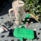 Green quilted phone case on a table with a floral mug, keys, and phone.