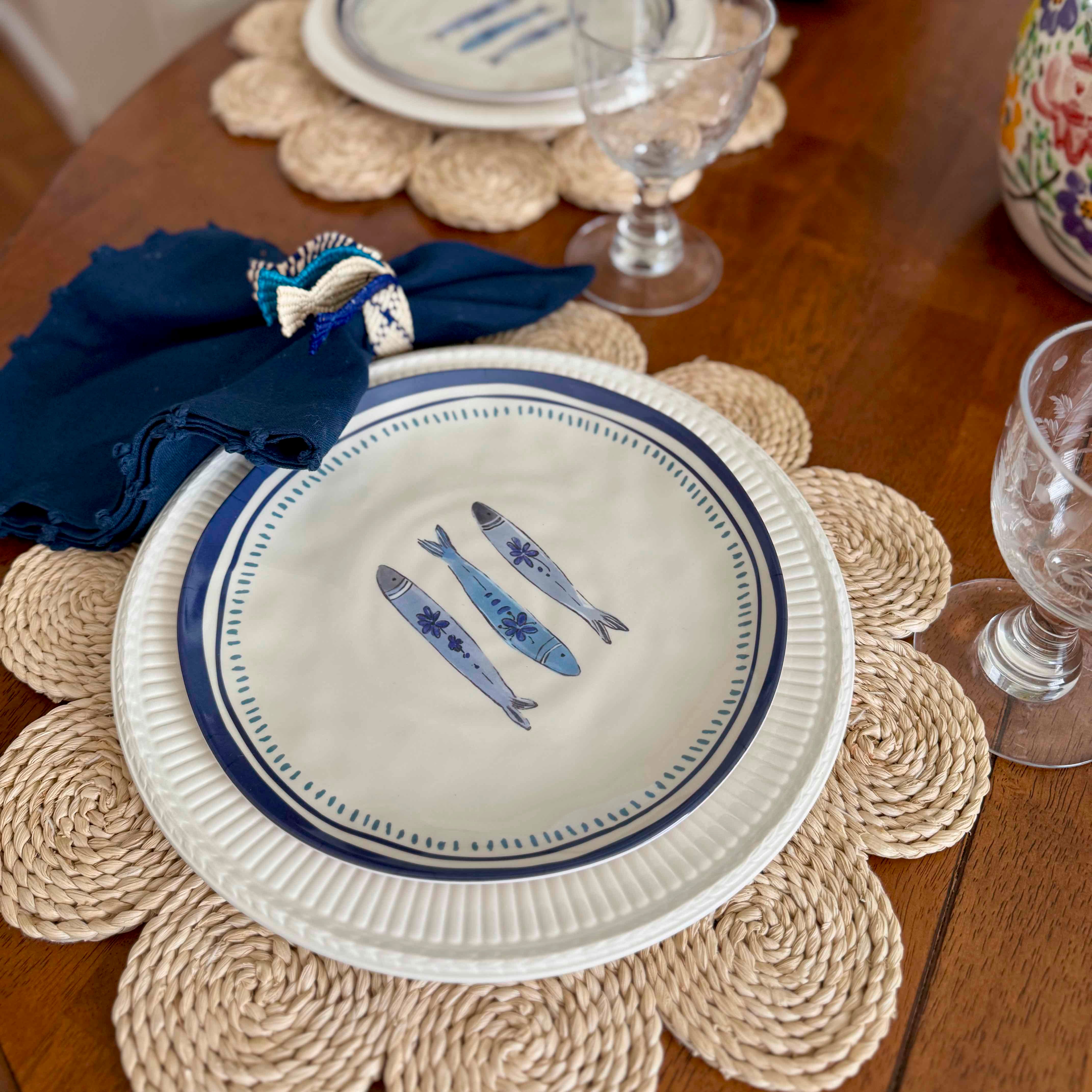 Table setting with a decorative plate featuring fish illustrations on a woven placemat.