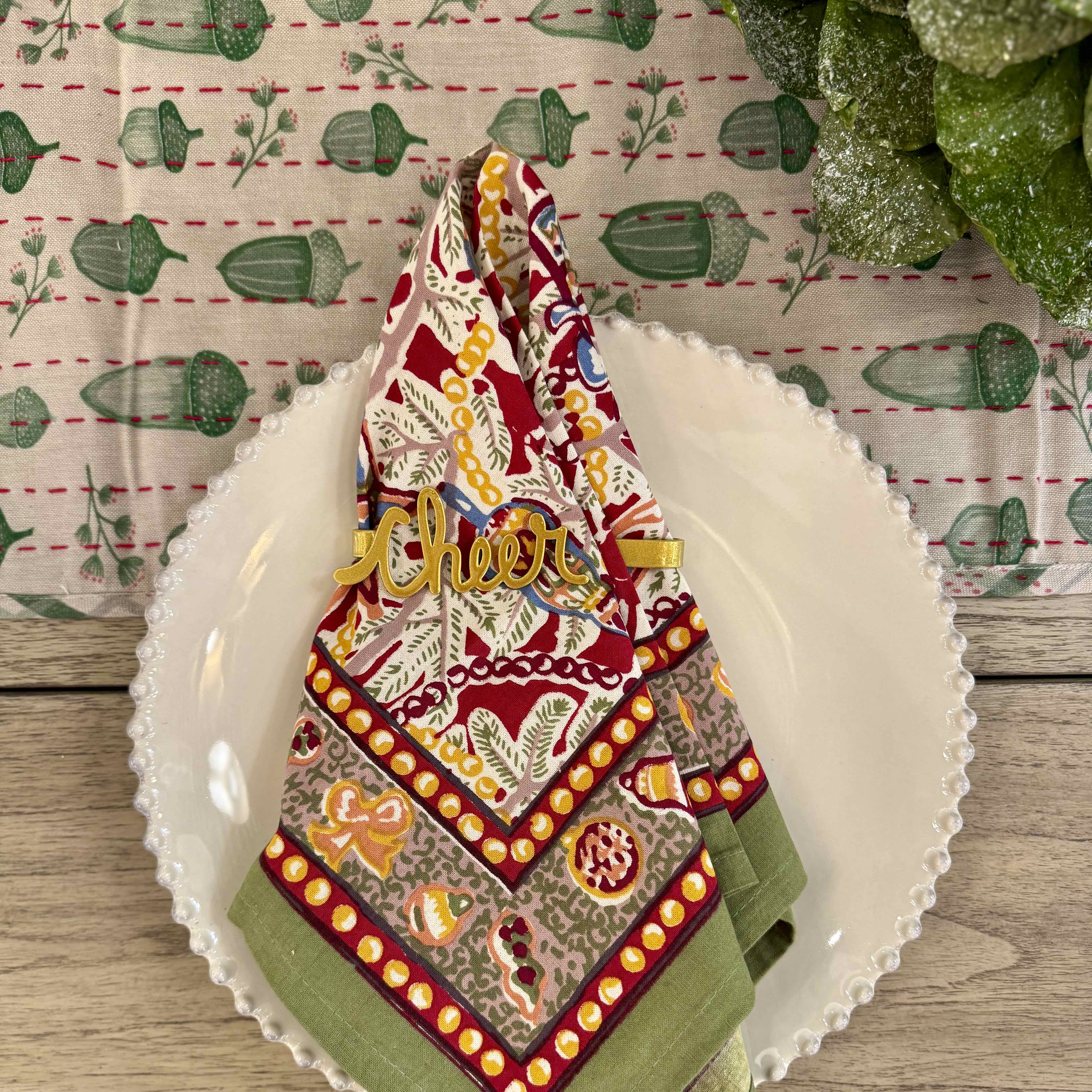 Decorative holiday towel with 'Cheer' on a white plate against a patterned background