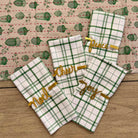 Set of green and white plaid towels with gold text on a wooden surface.