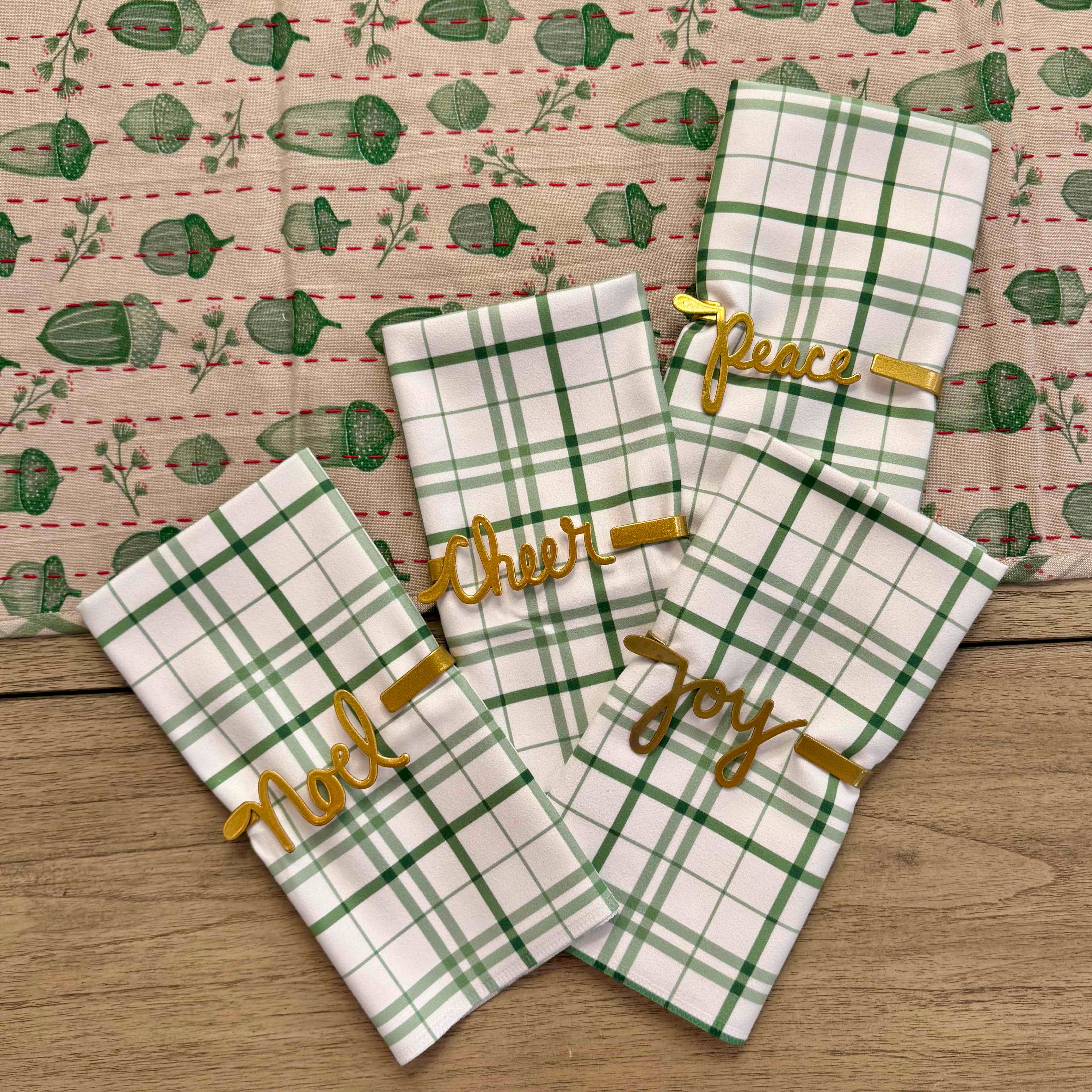Set of green and white plaid towels with gold text on a wooden surface.