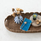 Wicker tray with decorative items including a striped vase, wooden spoon, and cookies on a light background