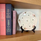 Decorative plate on a stand next to books on a wooden shelf