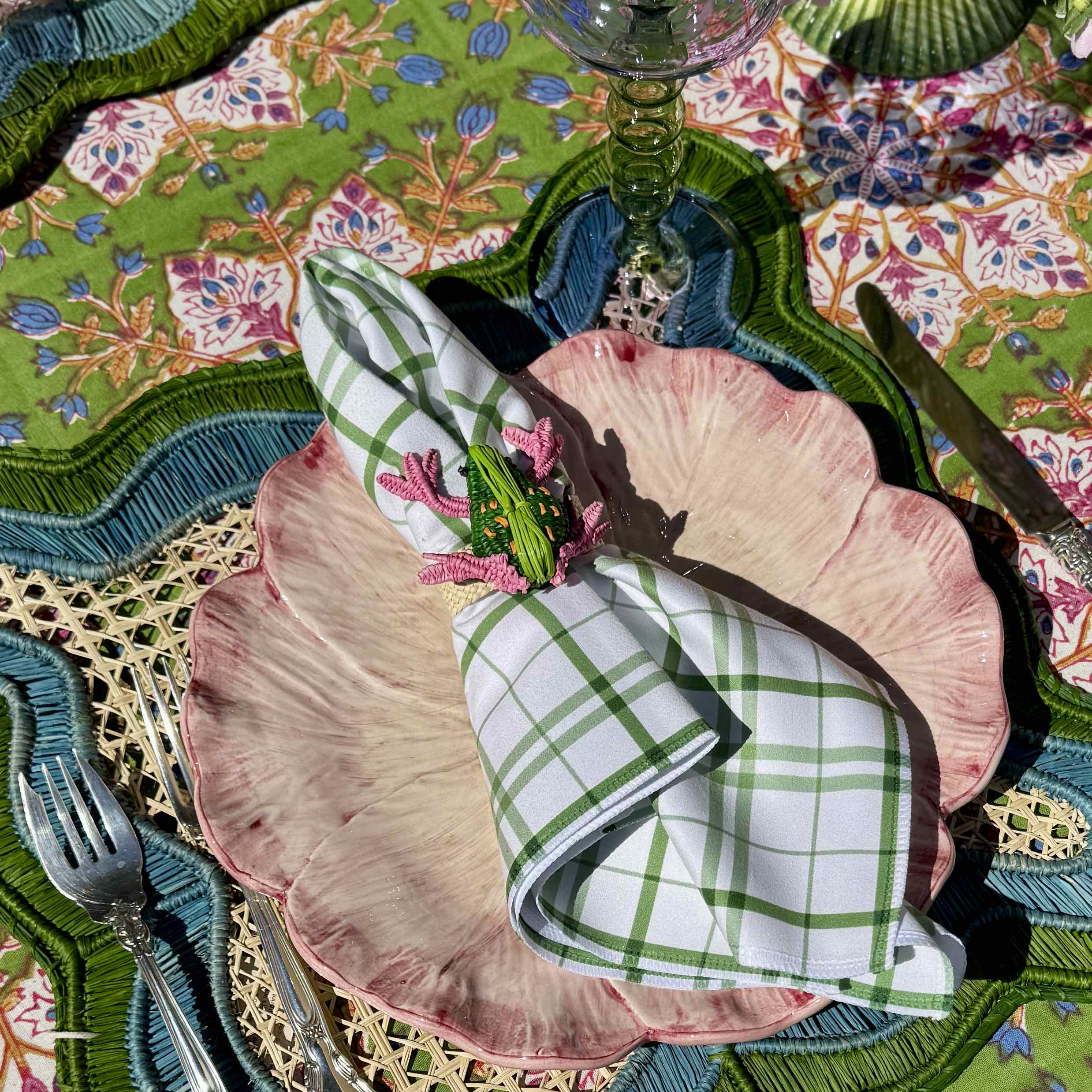 Decorative table setting with pink plates, green checkered napkins, and a colorful tablecloth.