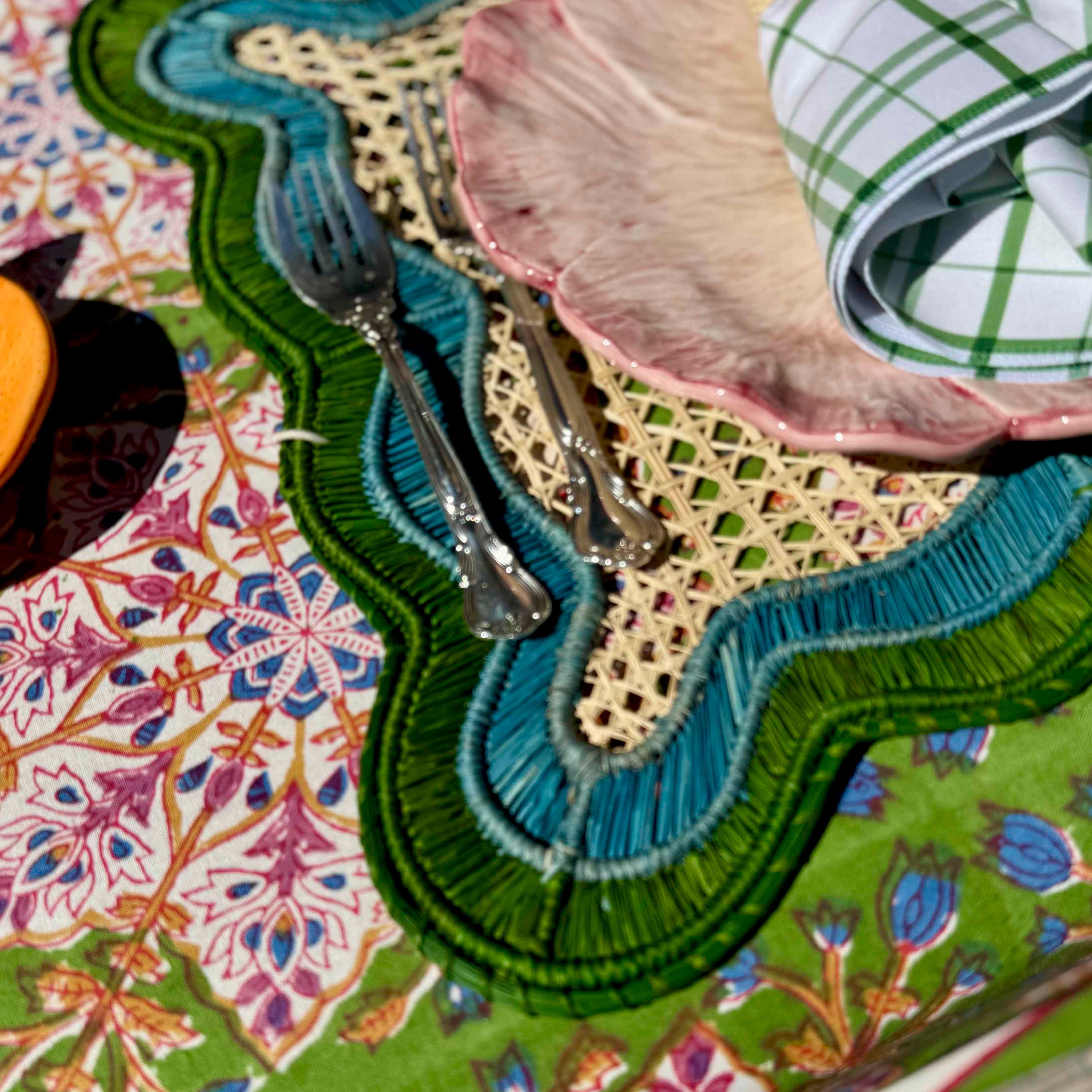 Colorful table setting with patterned placemats, cutlery, and napkins on a floral tablecloth.