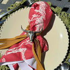 Red napkin with white patterns and tassels on a table setting with a fork and knife.