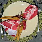 Decorative plate with a red napkin featuring white patterns and gold accents, on a green doily.