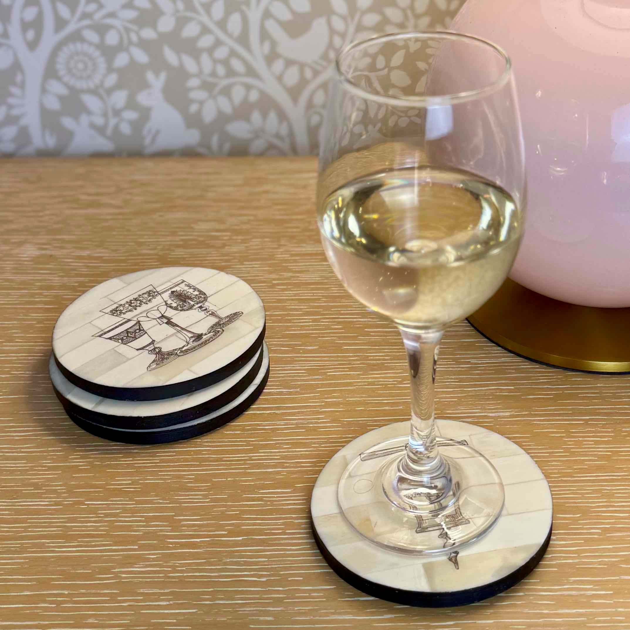 Stack of coasters with a ship design next to a glass of white wine on a coaster.