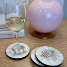 Wine glass with white wine on a table with decorative coasters featuring illustrations.