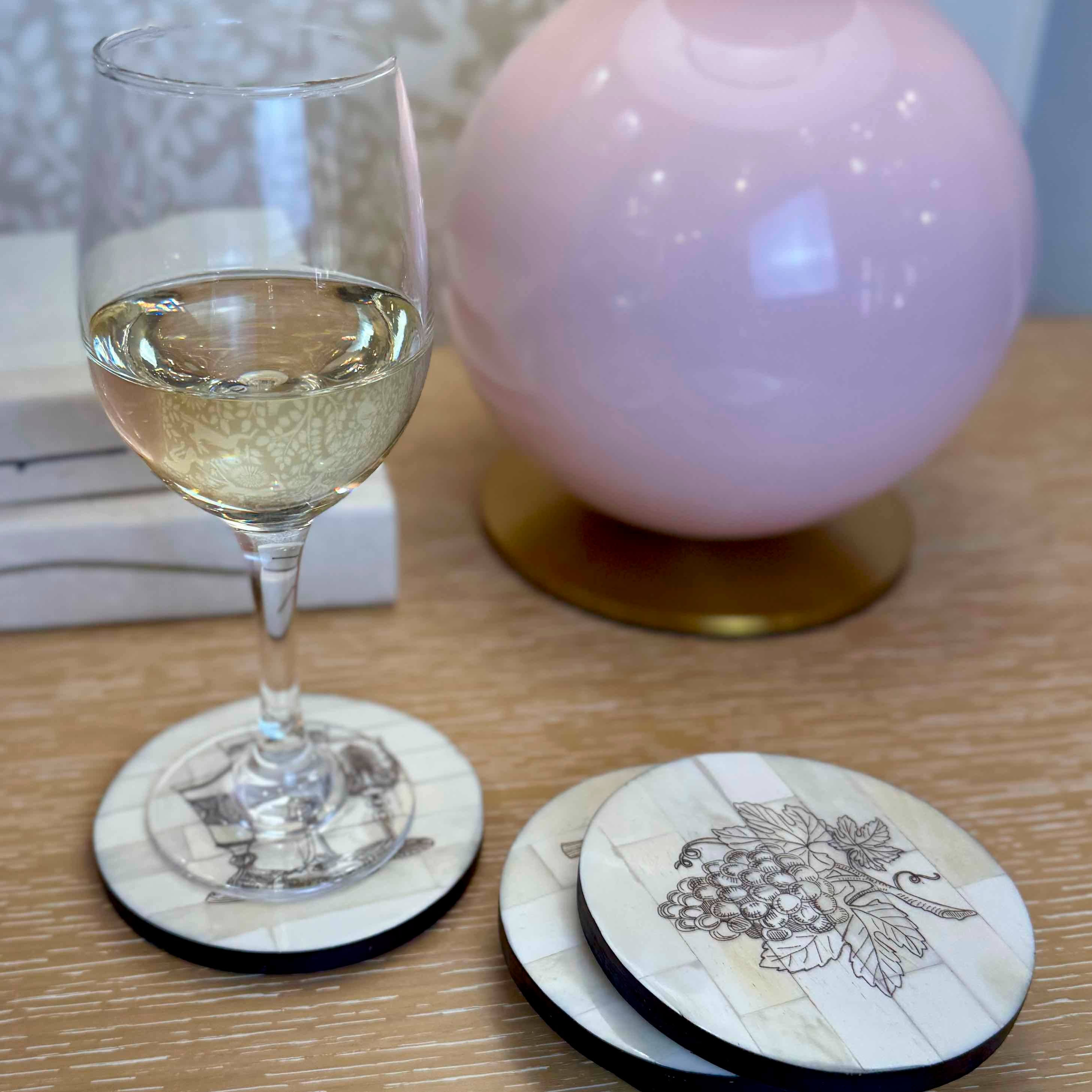 Wine glass with white wine on a table with decorative coasters featuring illustrations.