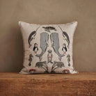 A square decorative throw pillow with an embroidered marine life pattern, resting on a rustic wooden surface against a textured beige wall.