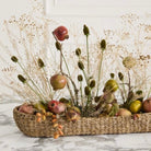 Decorative arrangement with fruits and flowers in a woven basket on a marble surface.