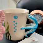 Two ceramic mugs with seahorse handles on a kitchen counter with a teapot and tea bags in the background.