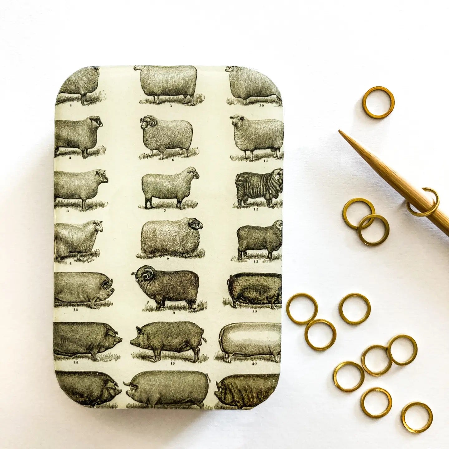 Rectangular tin with sheep pattern on a white background with gold rings and scissors.