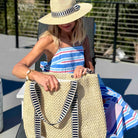 Woman in a striped dress and sun hat holding a straw bag outdoors.