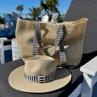 Beige straw bag and hat with striped bands on a table outdoors.
