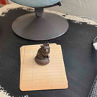 A small dark metallic rodent figurine, resembling a beaver or nutria, sitting on top of a stack of tan lined notepads on a dark desk.