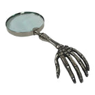A novelty magnifying glass with a metallic skeleton hand handle, shown on a plain white background.