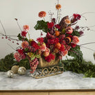 Decorative floral arrangement in a gold sleigh on a marble surface with greenery in the background.