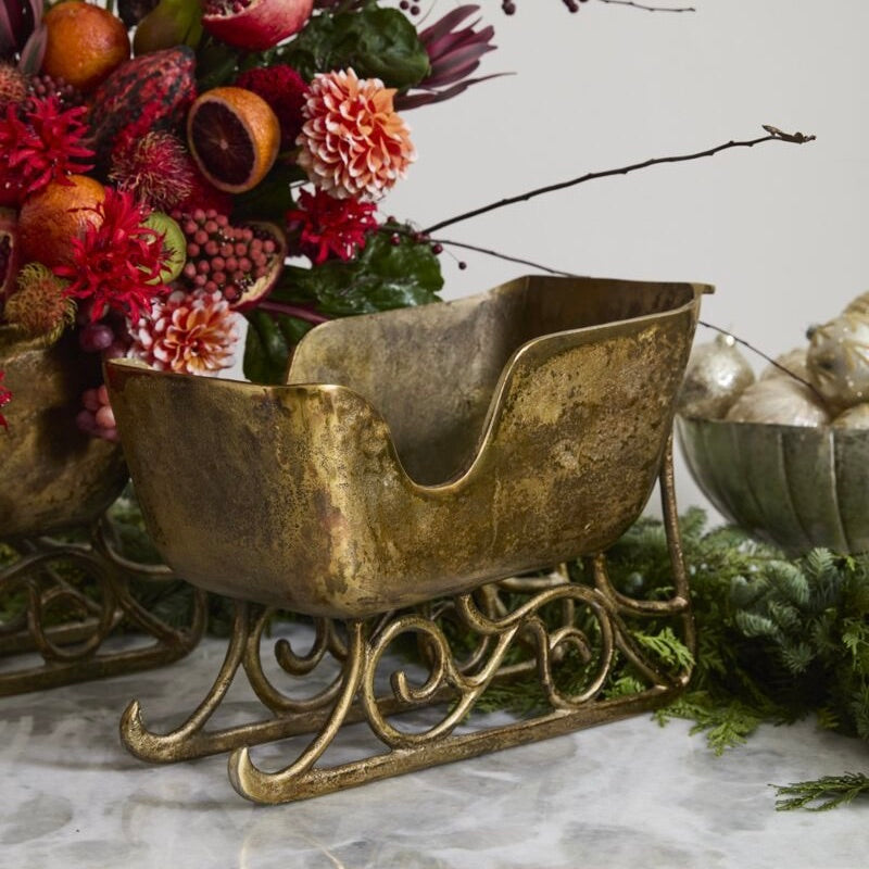 Decorative gold sleigh with floral arrangement and greenery on a marble surface