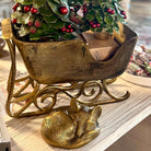 Decorative brass sleigh with a small dog figurine and Christmas tree on a wooden surface.