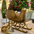 Decorative brass planter with a small tree and red berries on a wooden surface.