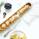 Wooden bread board with bread slices, a knife, and cheese on a white surface.