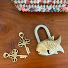 Gold fish-shaped padlock and two keys on a wooden surface