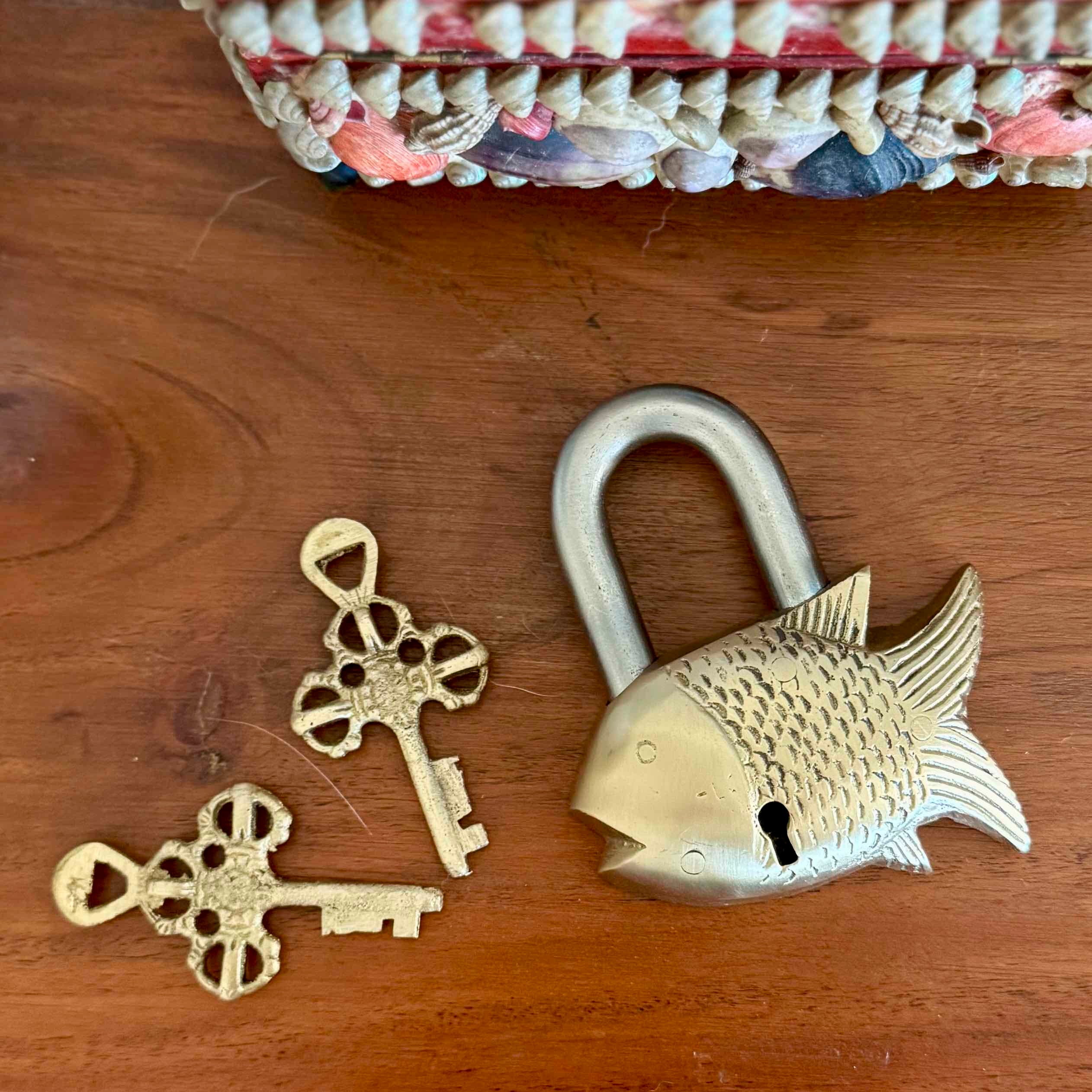 Gold fish-shaped padlock and two keys on a wooden surface