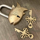 Brass fish-shaped padlock with two keys on a wooden surface