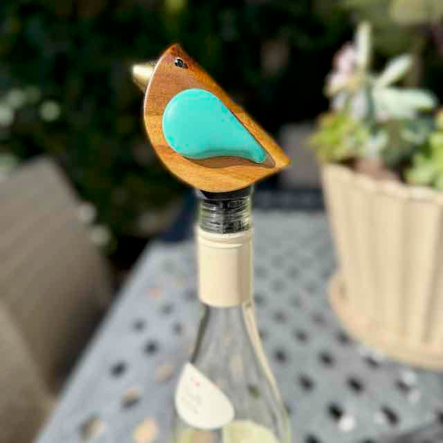 Bird-shaped bottle stopper on a wine bottle with a blurred outdoor background
