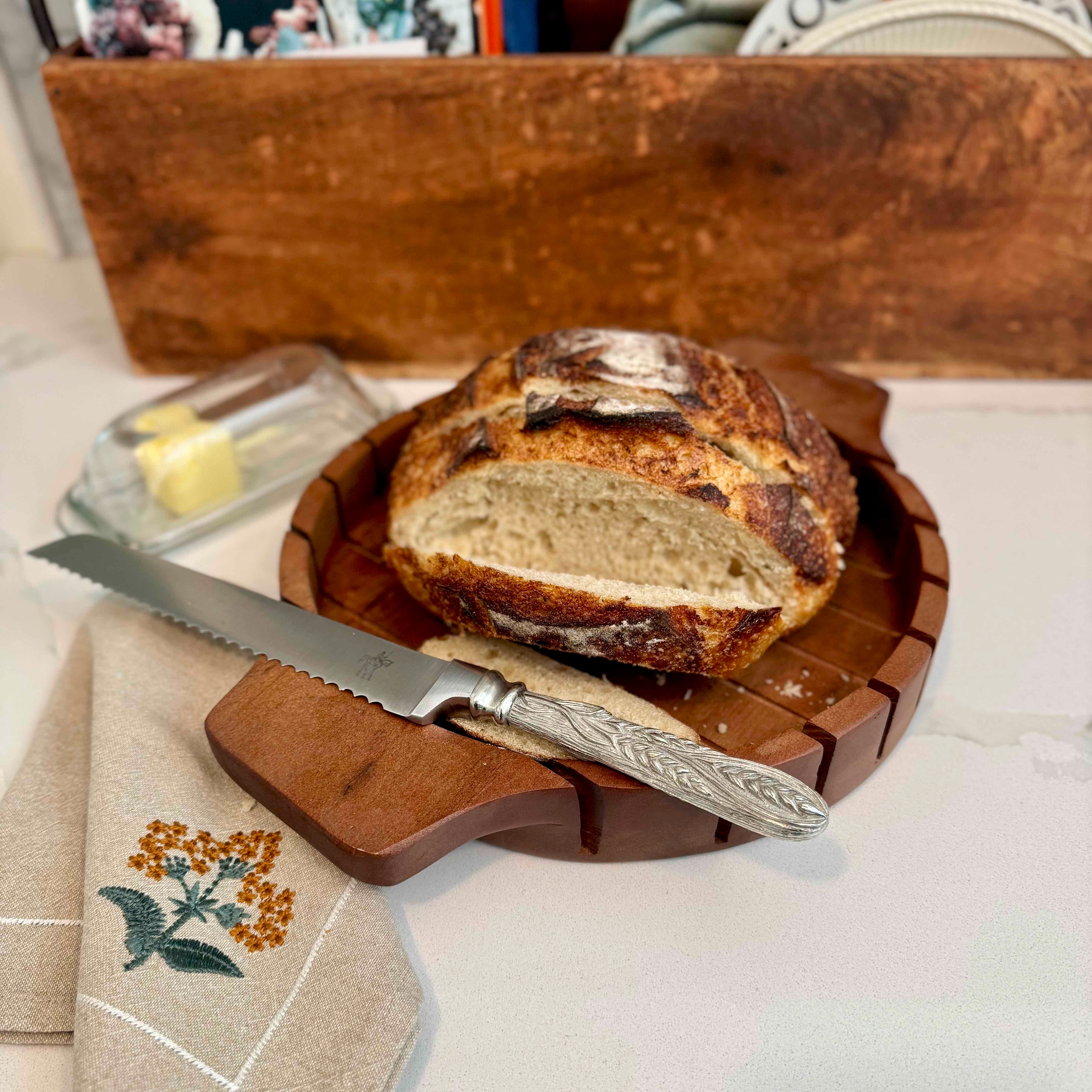 Loaf of bread on a wooden cutting board with a knife, on a tablecloth.