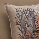 A close-up of a square linen throw pillow featuring a detailed embroidered design of bare trees, acorns, and orange pumpkins on a warm beige background.
