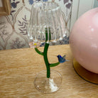 Decorative glass object with a green stem and blue bird figure on a wooden surface.