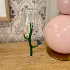 Decorative lamp with clear glass shade, green stem, and small blue bird on a wooden surface.