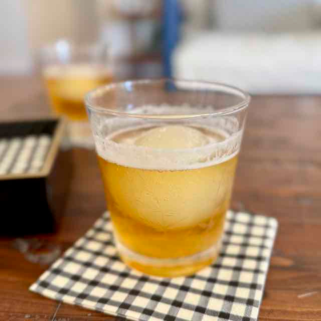 Clear glass of beer with foam on a checkered napkin on a wooden table.