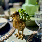 Gold bird figurine on a decorative table setting with a green vase and glassware.