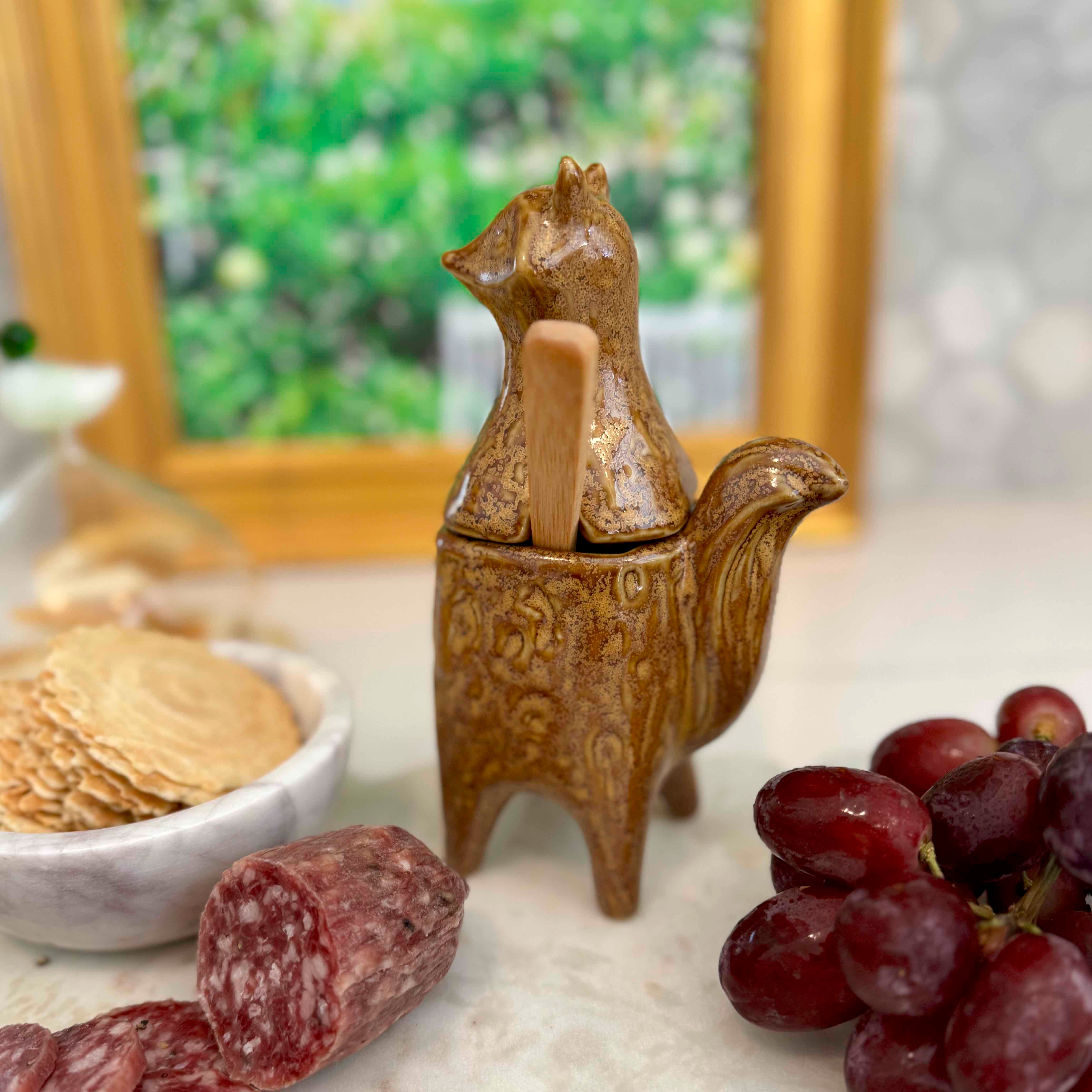 Decorative ceramic fox-shaped container on a table with grapes and salami.