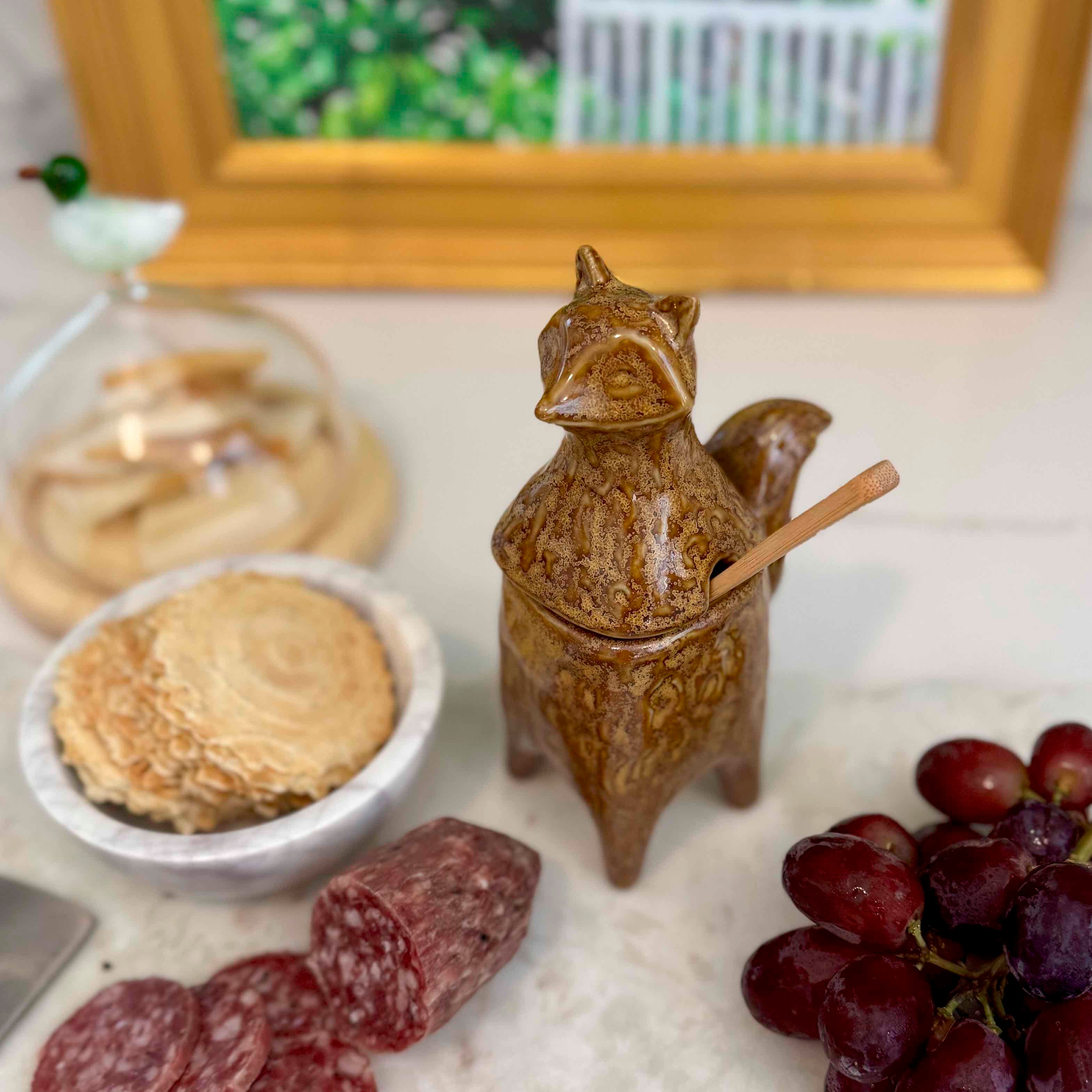 Ceramic container shaped like a fox with a wooden stick, surrounded by snacks on a marble surface.