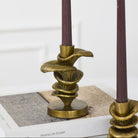 Two ornate gold-toned spiral candle holders with dark plum taper candles, styled on top of a book against a white paneled wall.