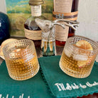 Two glasses of whiskey with a decorative deer head decanter and bottles in the background.