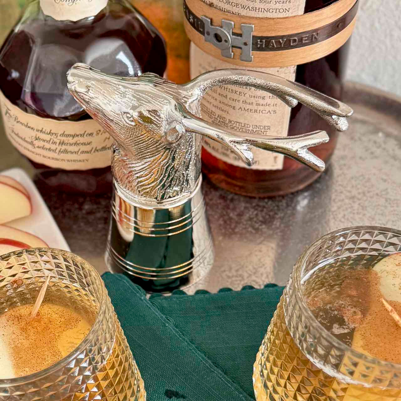 Bottle stopper with deer design in front of whiskey bottles on a table.