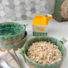 Green ceramic bowls with oats and a yellow milk carton on a marble surface