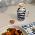 Ceramic pitcher with blue leaf pattern on a table with a plate of food and fork.