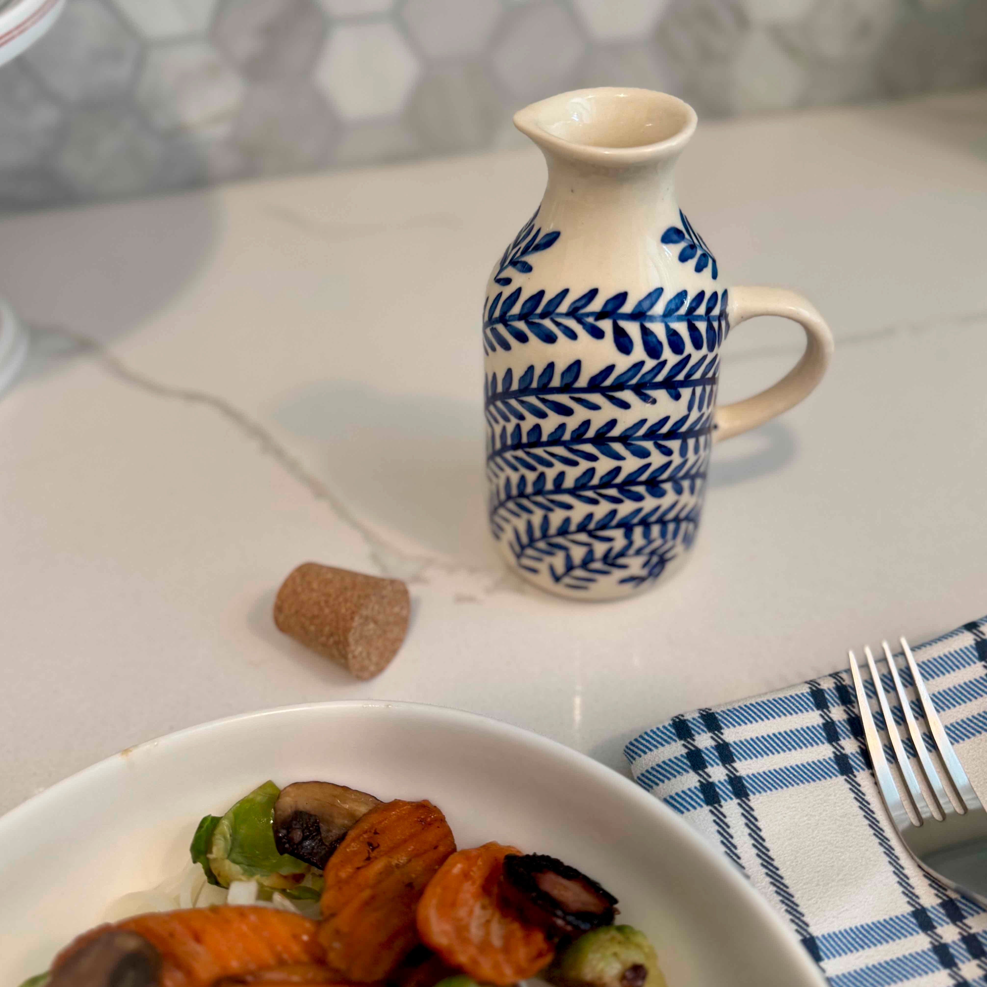 Ceramic pitcher with blue leaf pattern on a table with a plate of food and fork.