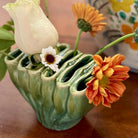 Green ceramic vase with flowers on a wooden surface