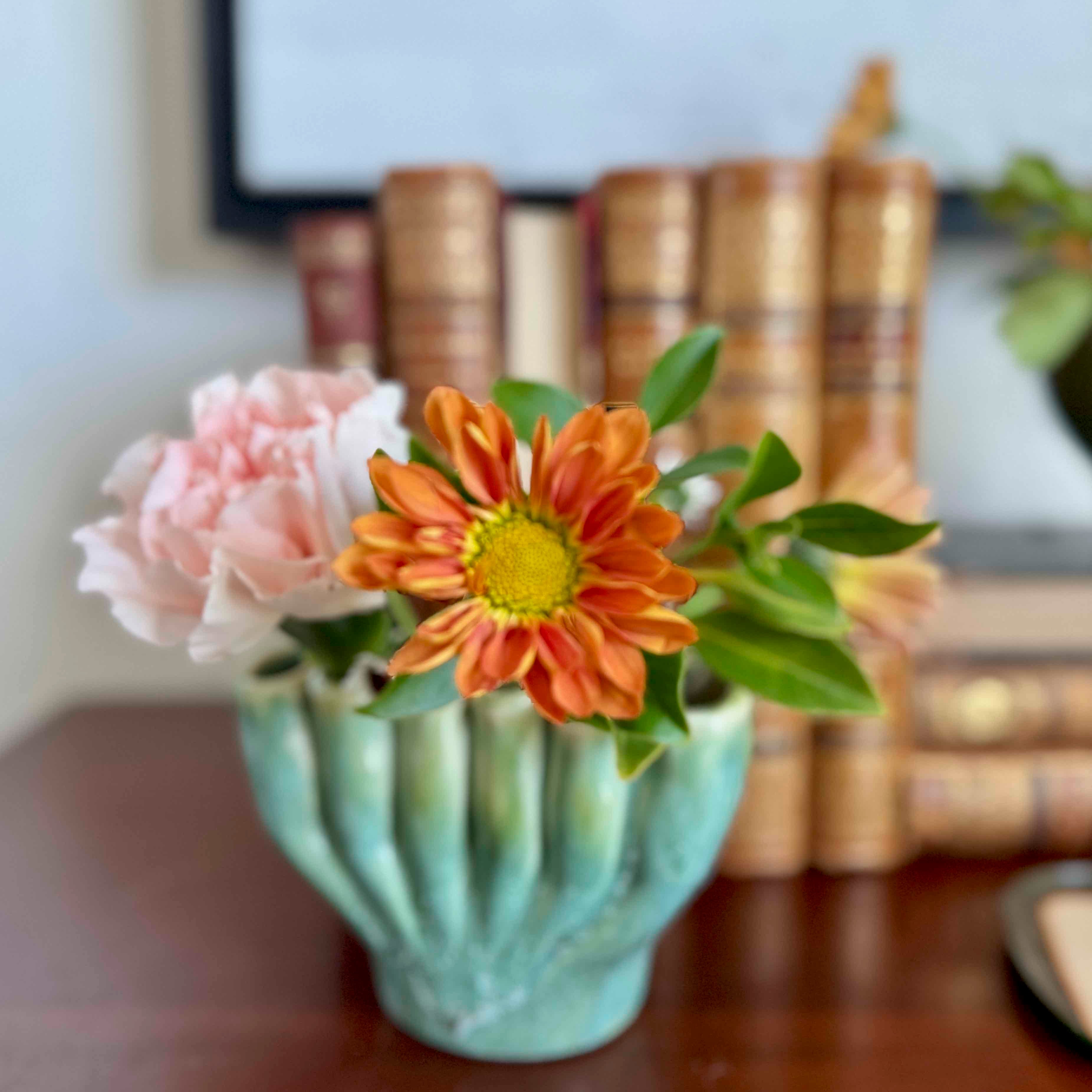 Decorative vase with flowers in front of books on a shelf