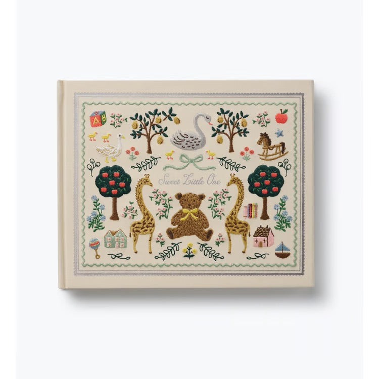 A square baby keepsake album with a cream-colored cover and a detailed, colorful embroidered-style illustration of a nursery scene featuring a teddy bear, giraffes, trees, and a swan. The text 'Save the Little One' is embroidered in the center.