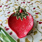 Red ceramic strawberry-shaped dish with green leaves on a floral tablecloth