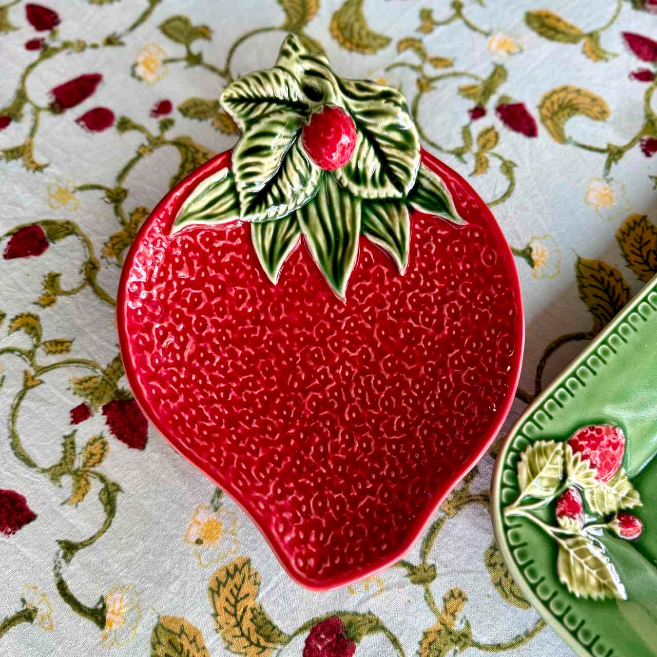 Red ceramic strawberry-shaped plate with green leaves on a patterned surface